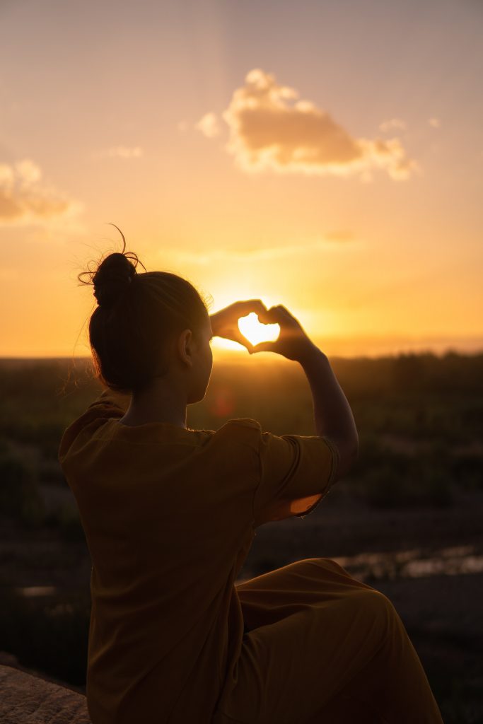 Woman showing heart sign hand - gratitudes in the sunset